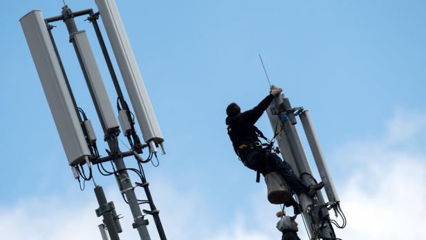 Ein Arbeiter klettert auf einen Mobilfunkmast vor blauem Himmel.