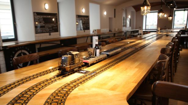 Ein Miniaturzug transportiert Getränke auf einer langen Holztischplatte in einem Restaurant.