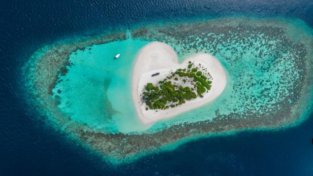 Eine herzförmige Insel mit weißem Sand und grüner Vegetation, umgeben von türkisfarbenem Wasser.