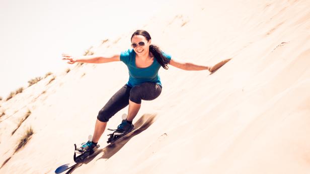 Eine Frau fährt mit einem Sandboard eine Düne hinunter.