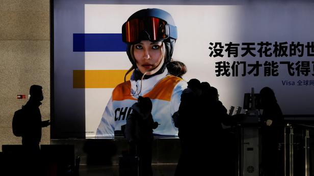 People line up to board a train near an image of freestyle skier Eileen Gu at a railway station ahead of the Beijing 2022 Winter Olympics, in Beijing