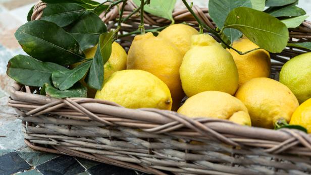 Ein Korb voller Zitronen mit Blättern steht auf einem Tisch.