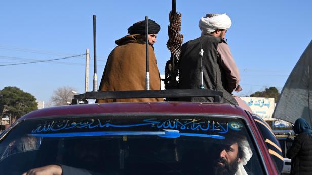 Zwei Männer mit Turban sitzen auf einem Auto mit einem Maschinengewehr.