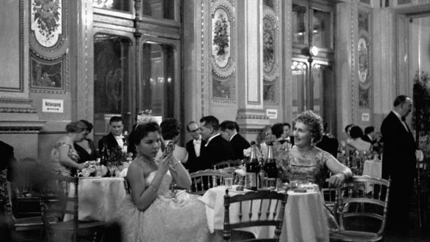 Gäste sitzen an Tischen bei einer formellen Veranstaltung in einem eleganten Saal.