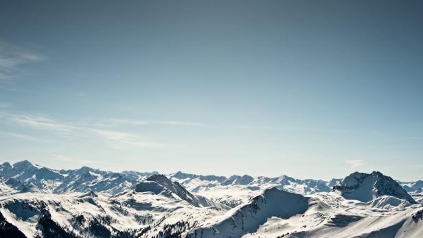 Eine weite, schneebedeckte Berglandschaft unter einem hellblauen Himmel.