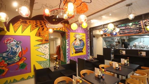 Innenansicht eines Restaurants mit farbenfrohen Wandmalereien und Tischen.
