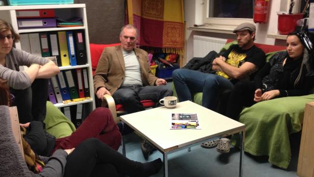 Eine Gruppe von Menschen sitzt in einem Raum um einen Tisch herum.