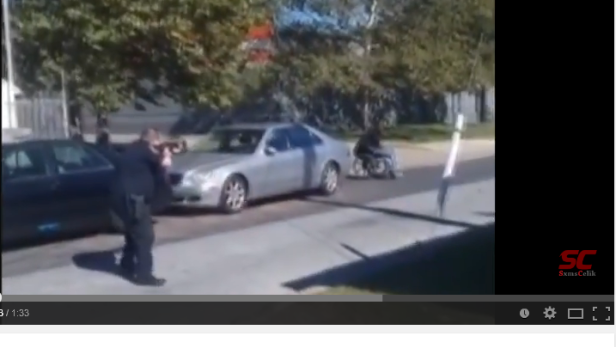 Ein Polizist zielt mit einer Waffe auf einen Mann im Rollstuhl.