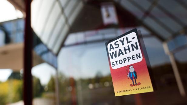 Ein Aufkleber mit der Aufschrift „Asyl-Wahn stoppen“ klebt an einer Scheibe.
