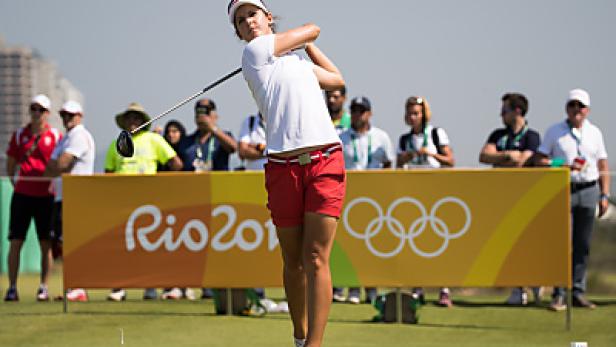Eine Golferin schwingt ihren Schläger vor dem Hintergrund der Olympischen Ringe von Rio 2016.
