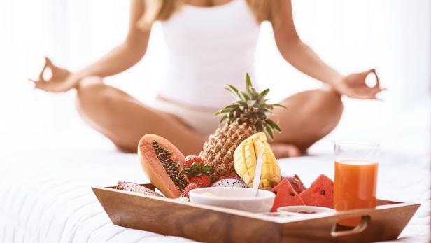 Eine Frau meditiert mit einem Tablett voller tropischer Früchte vor sich.