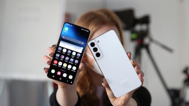 Eine Person hält ein Samsung-Smartphone mit geöffnetem App-Bildschirm und die Rückseite eines zweiten Samsung-Smartphones in die Kamera.