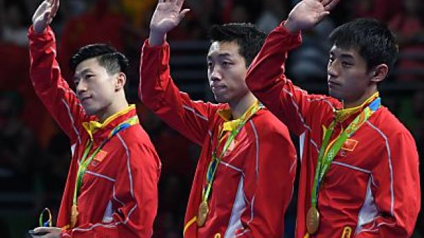 Drei chinesische Tischtennisspieler mit Goldmedaillen winken dem Publikum zu.