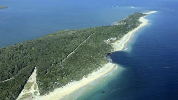 Luftaufnahme einer bewaldeten Insel mit Sandstrand und blauem Meer.