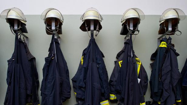 Mehrere Feuerwehrhelme und Uniformen hängen an Wandhaken in einer Reihe.