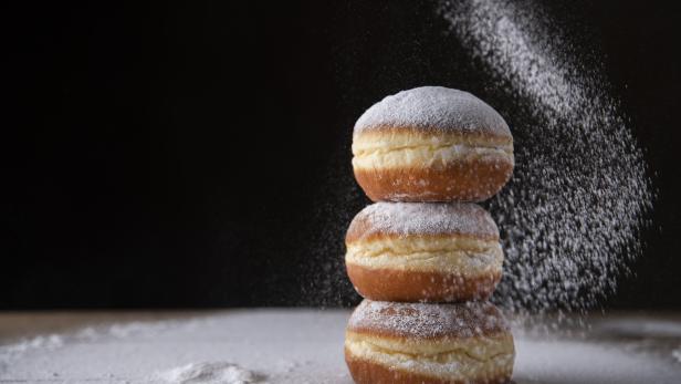 European donut sprinkled with powdered sugar on black background.