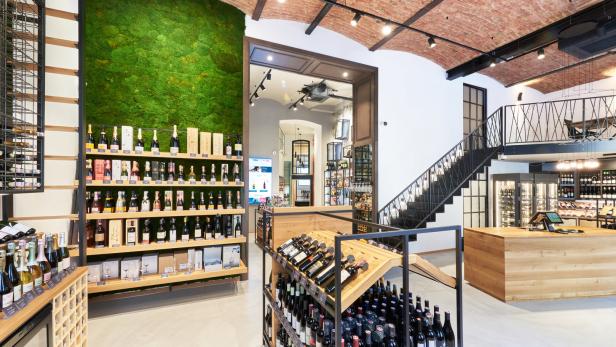 Innenansicht eines Weinladens mit Regalen voller Flaschen und einer Mooswand.