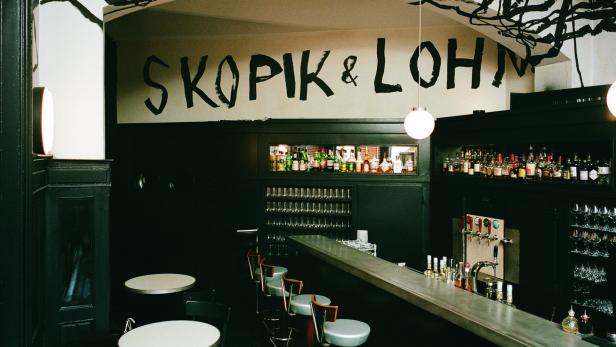 Innenansicht der Bar Skopic & Lohn mit dunkler Einrichtung und dem Schriftzug an der Wand.