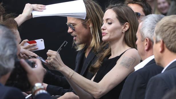 Angelina Jolie und Brad Pitt geben Autogramme umringt von Fans.