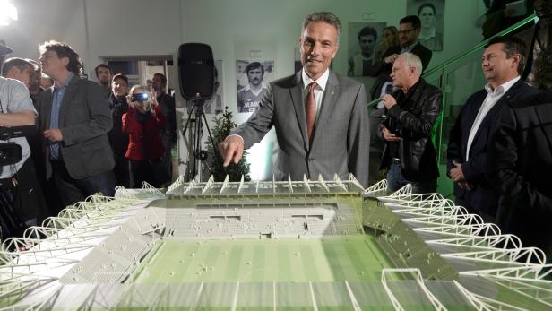 Ein Mann im Anzug präsentiert ein Modell eines Fußballstadions.