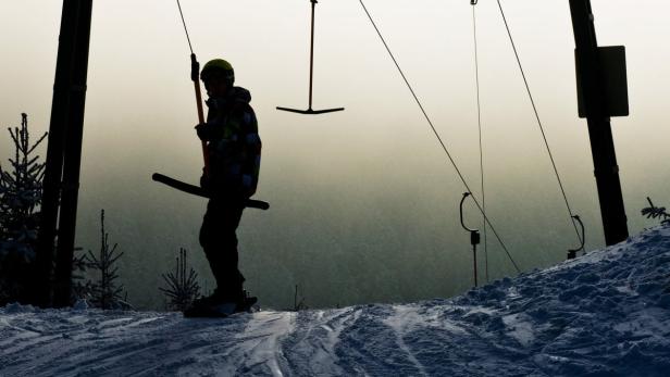 Ein Skifahrer steht am Skilift mit einem Schleppliftbügel in der Hand.