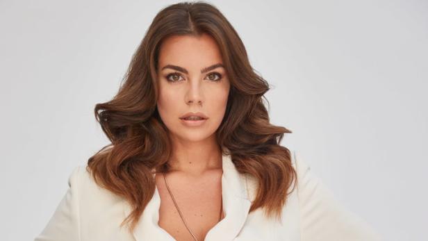 Eine Frau mit braunen Haaren trägt einen weißen Hosenanzug.