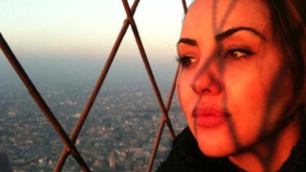 Eine Frau blickt durch das Gitter des Eiffelturms auf Paris.