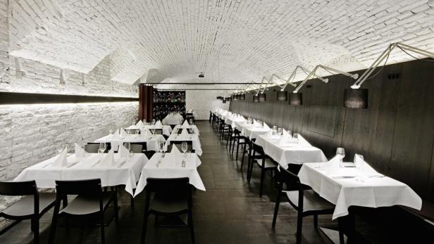 Ein Speisesaal mit gedeckten Tischen unter einem Gewölbe aus weißen Ziegeln.