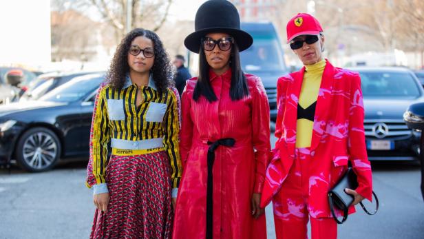 Drei Frauen posieren in farbenfrohen Outfits, darunter Ferrari-Logos, für ein Foto.