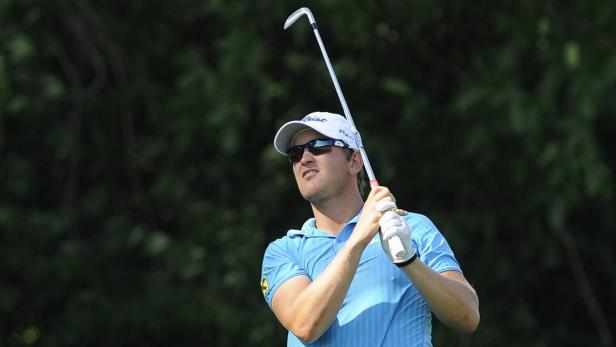 Ein Golfspieler schwingt seinen Schläger vor einem Hintergrund aus Bäumen.