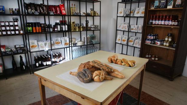 In einem Laden steht ein Tisch mit Brot und Brötchen vor Regalen mit Lebensmitteln.