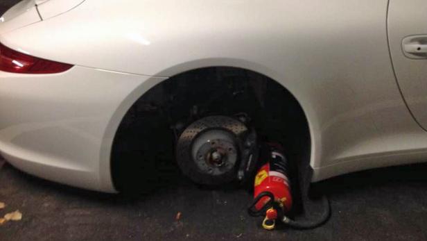Ein weißer Sportwagen mit abmontiertem Rad und einem roten Feuerlöscher daneben.