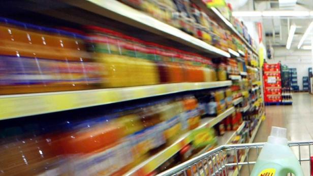 Ein Einkaufswagen fährt an vollen Regalen in einem Supermarkt vorbei.