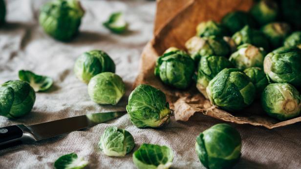 Rosenkohl liegt neben einem Messer und einer Papiertüte auf einem Tisch.