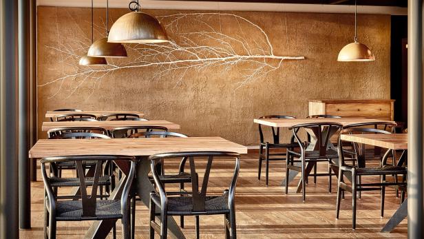 Ein Restaurant mit Holztischen, schwarzen Stühlen und einer Wanddekoration in Form eines Astes.