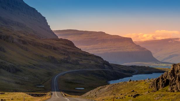 Eine Straße schlängelt sich durch eine hügelige Landschaft am Wasser entlang.