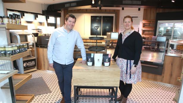Ein Mann und eine Frau stehen in einem Geschäft neben einem Tisch mit Kaffeepackungen.