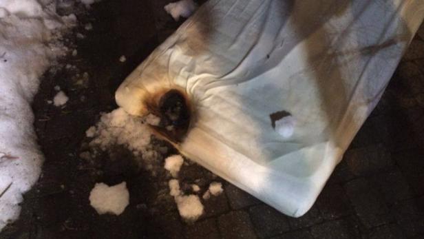Eine Matratze mit einem Brandloch liegt im Schnee.