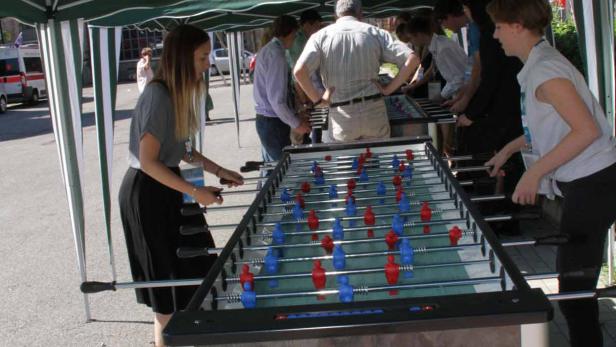 Mehrere Personen spielen an einem Tischfußballspiel unter einem grünen Zelt.