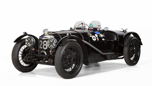 Ein schwarzer Oldtimer-Rennwagen mit der Nummer 28 steht vor einem weißen Hintergrund.