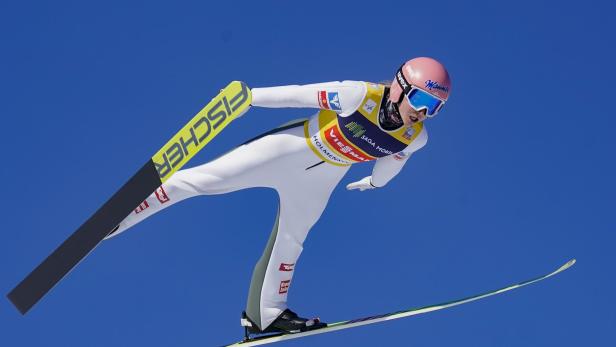 Eine Skispringerin in der Luft vor blauem Himmel.