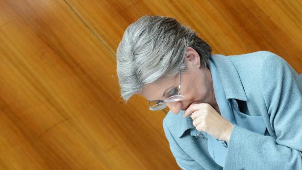 Eine Frau mit Brille und grauem Haar schaut nach unten und berührt ihr Gesicht.