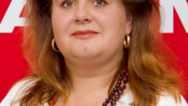 Eine Frau mit braunen Haaren und einer Halskette vor einem roten Hintergrund.