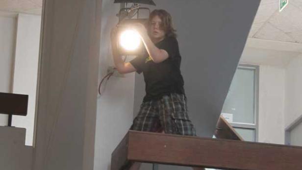 Eine Person justiert eine helle Bühnenlampe, die an einer Wand montiert ist.