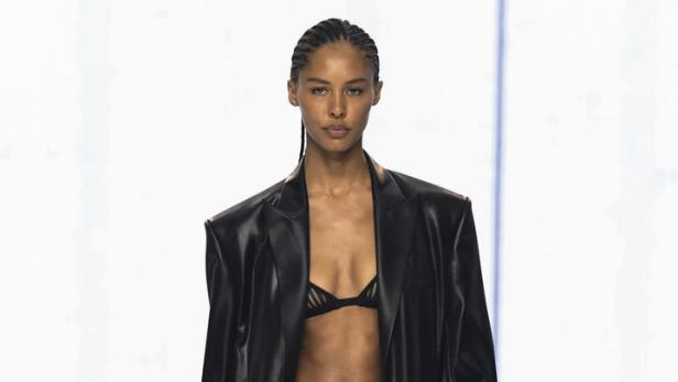 Eine Frau in einem schwarzen Outfit auf einem Laufsteg präsentiert ein Kleidungsstück.