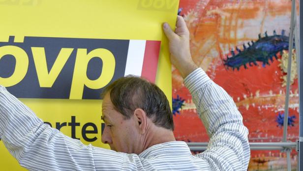 Ein Mann befestigt ein gelbes Wahlplakat der ÖVP.