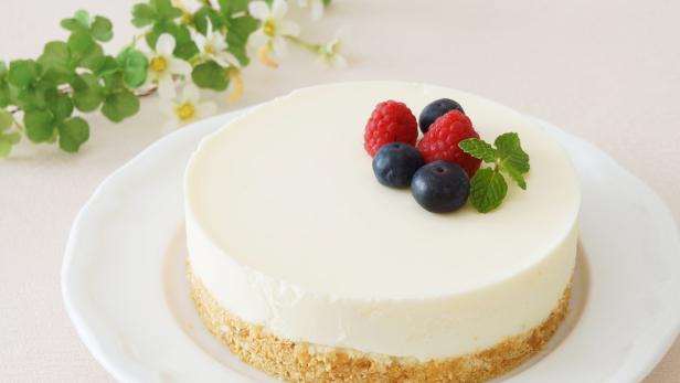 Ein Käsekuchen ist mit Blaubeeren, Himbeeren und Minze garniert.