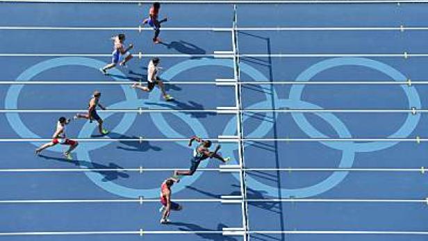 Athleten laufen ein Hürdenrennen auf einer blauen Bahn mit den olympischen Ringen.
