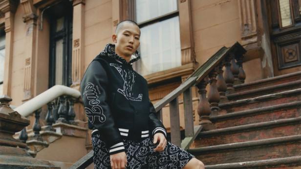 Ein Mann in einer Louis Vuitton Jacke und Shorts steht auf einer Treppe vor einem Gebäude.