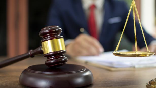 Ein Richterhammer und eine goldene Waage auf einem Schreibtisch.